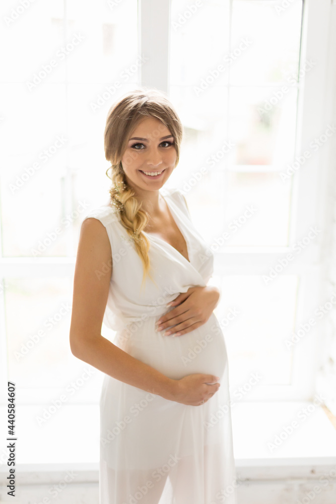 pregnant woman in a white dress hugs her belly with her hands