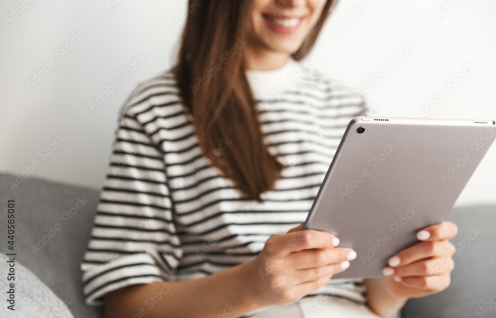 Cropped shot of smiling woman using tablet, girl reading or watching smth online on her gadget while sitting at home on sofa Cropped shot of smiling woman using tablet, girl reading or watching smth online on her gadget while sitting at home on sofa