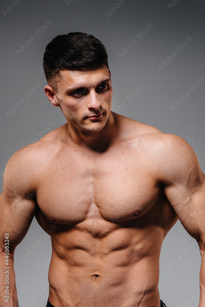 A young sexy athlete with perfect abs poses in the studio topless in jeans on the background. Healthy lifestyle, proper nutrition, training programs and nutrition for weight loss.