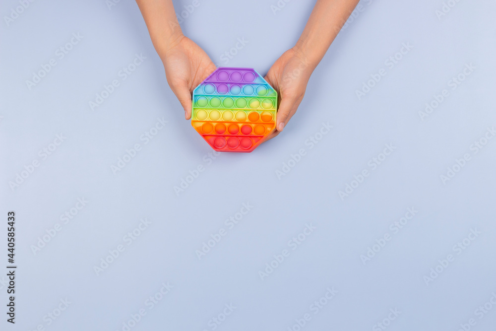 Kid hands holding new trendy pop it fidget toy on blue background. Push pop-it fidgeting game helps relieve stress, anxiety, autism, provide sensory and tactile experience for children Kid hands holding new trendy pop it fidget toy on blue background. Push pop-it fidgeting game helps relieve stress, anxiety, autism, provide sensory and tactile experience for children