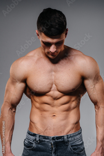 A young sexy athlete with perfect abs poses in the studio topless in jeans on the background. Healthy lifestyle, proper nutrition, training programs and nutrition for weight loss.