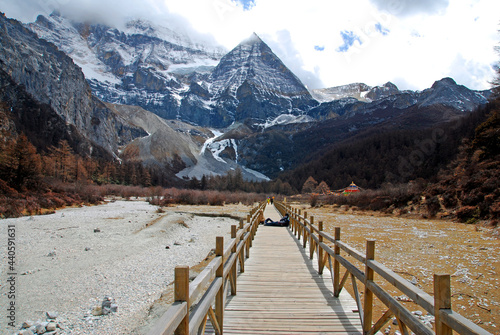 Landscape Long wood bridge to Pearl Lake with Chenrezig (Xiannairi) Holy snow Mountain background at Yading winter season. It is the highest peak in Daocheng Country,China - hikes to epic mountains  photo