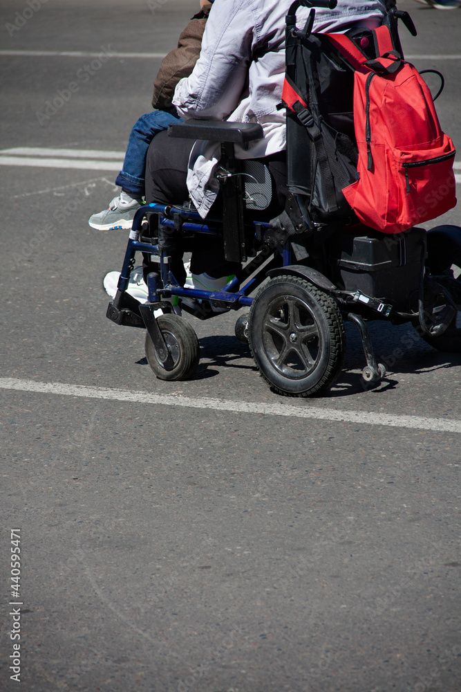 Back view of young disabled woman.View of the legs of a woman sitting in a wheelchair with a child on her lap.Rear view of a young woman in a wheelchair during a walk in the center of the city, a plac