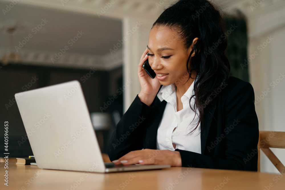 Businesswoman afro smiles manager working on laptop and tablet. The financier calls a project colleague on the phone. The lawyer sits in a modern rented office.