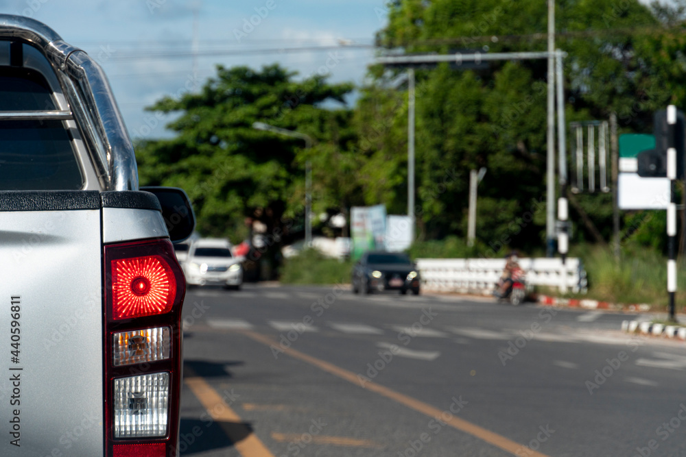Back side of pick up car silver color on the asphalt road. Blurred vision of road traffic lights at the intersection. during the day in Thailand.