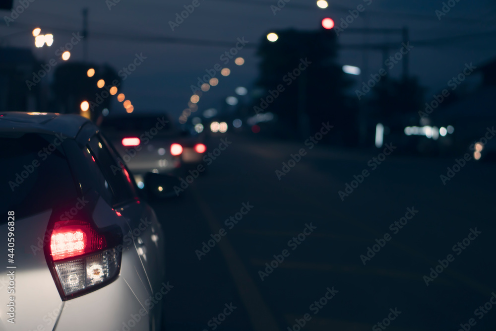 Abstract and blurred of rear side white car driving on the road in the city. During night time with bokeh of light pole on front.