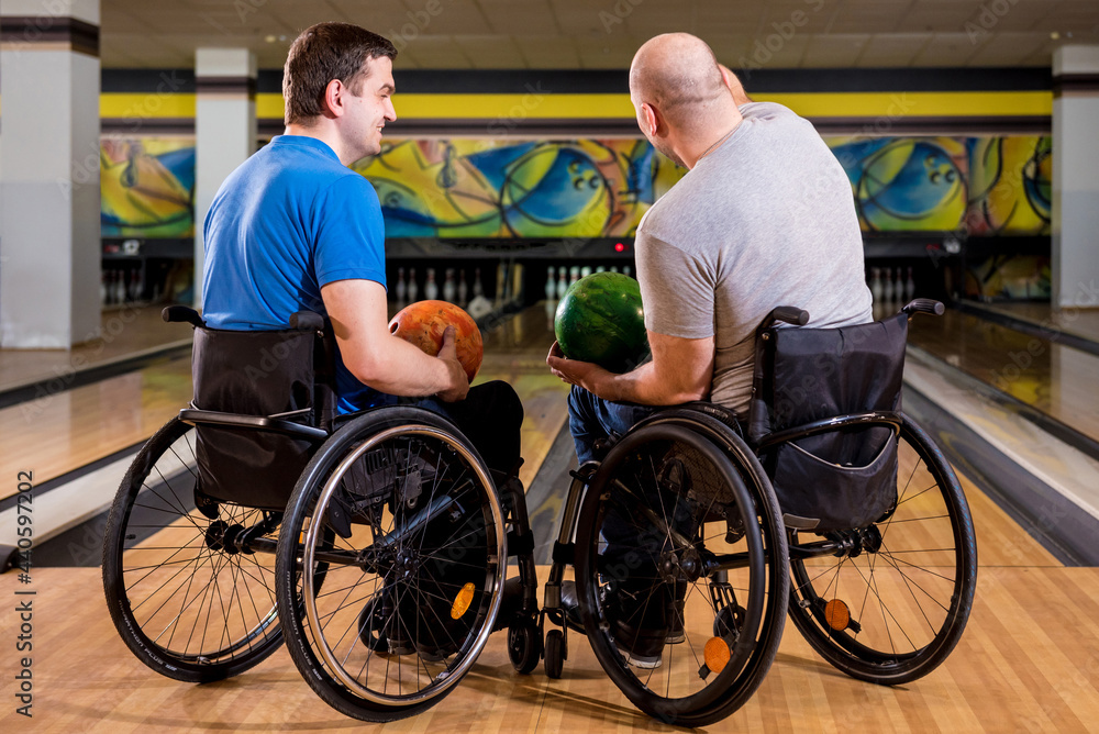 Obraz premium Two young disabled men in wheelchairs playing bowling in the club