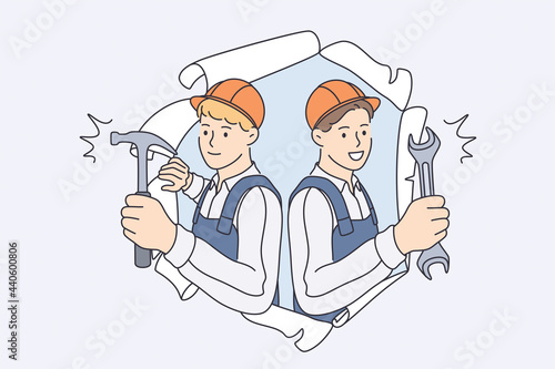 Repairmen during construction work concept. Young smiling men workers in helmets and working uniform standing looking from damaged old wallpapers holding hammers in hands 