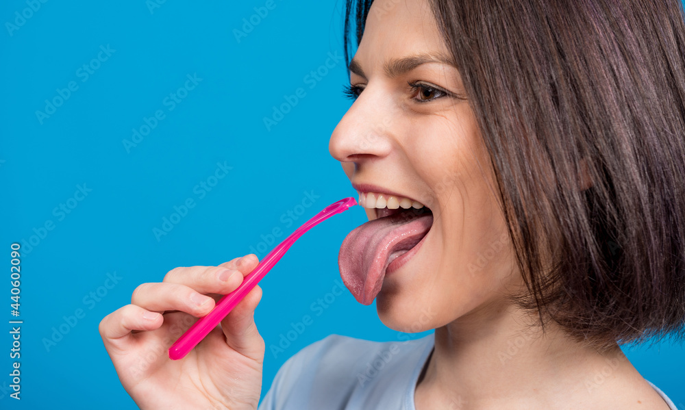 Beautiful happy young woman with tongue scraper on blank blue background Beautiful happy young woman with tongue scraper on blank blue background