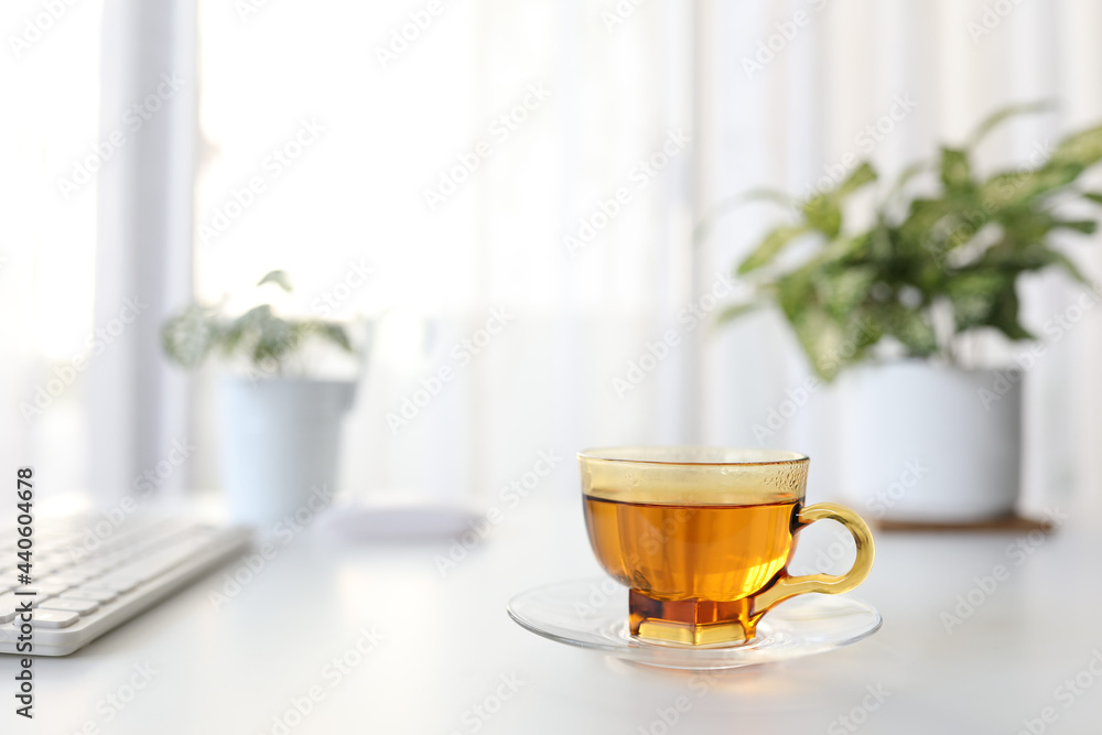 Tea in transparent cup on white desk table with keyboard and plant pot Tea in transparent cup on white desk table with keyboard and plant pot