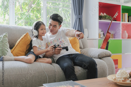 Two asian young father and adorable little girl daughter family enjoy playing game console together with happy smiling face at sofa living room on holiday weekend. Selective focus. © paepae stocker 