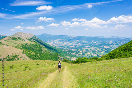 Hiking in the Montelago highlands, Marche, Italy. Woman walking in green landscape unique hills and mountains landscape. Summer outdoors activity. photo