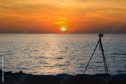 Digital professional camera stand on tripod photographing sea. Twilight sky background. Colorful Sunset sky and cloud. vivid sky in twilight time background. Fiery orange sunset sky. Beautiful