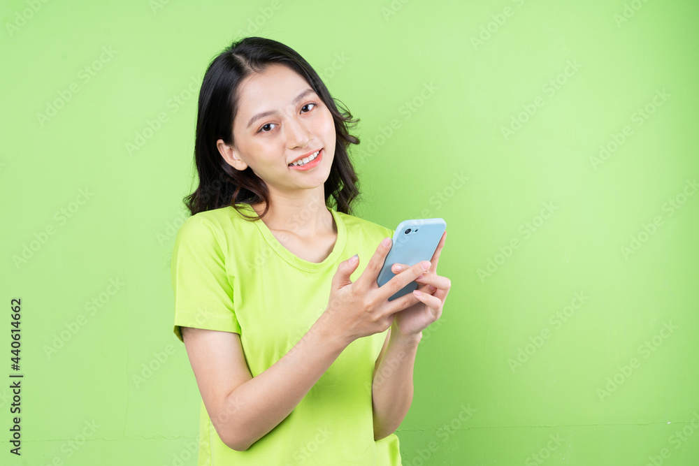 Image of young asian woman holding smartphone on green background Image of young asian woman holding smartphone on green background