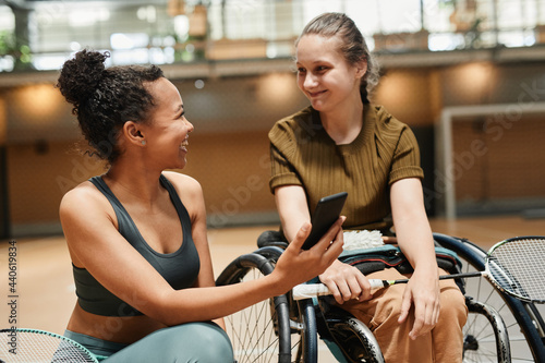 Portrait of smiling young woman in wheelchair talking to coach or teammate during sports practice at indoor court © Seventyfour