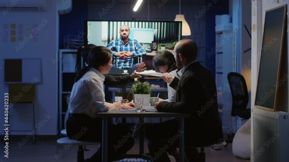 Multi ethnic businesspeople discussing with remote entrepreneur in wheelchair during online videocall conference at night in company meeting office room. Diverse focused teamwork brainstorming ideas Multi ethnic businesspeople discussing with remote entrepreneur in wheelchair during online videocall conference at night in company meeting office room. Diverse focused teamwork brainstorming ideas