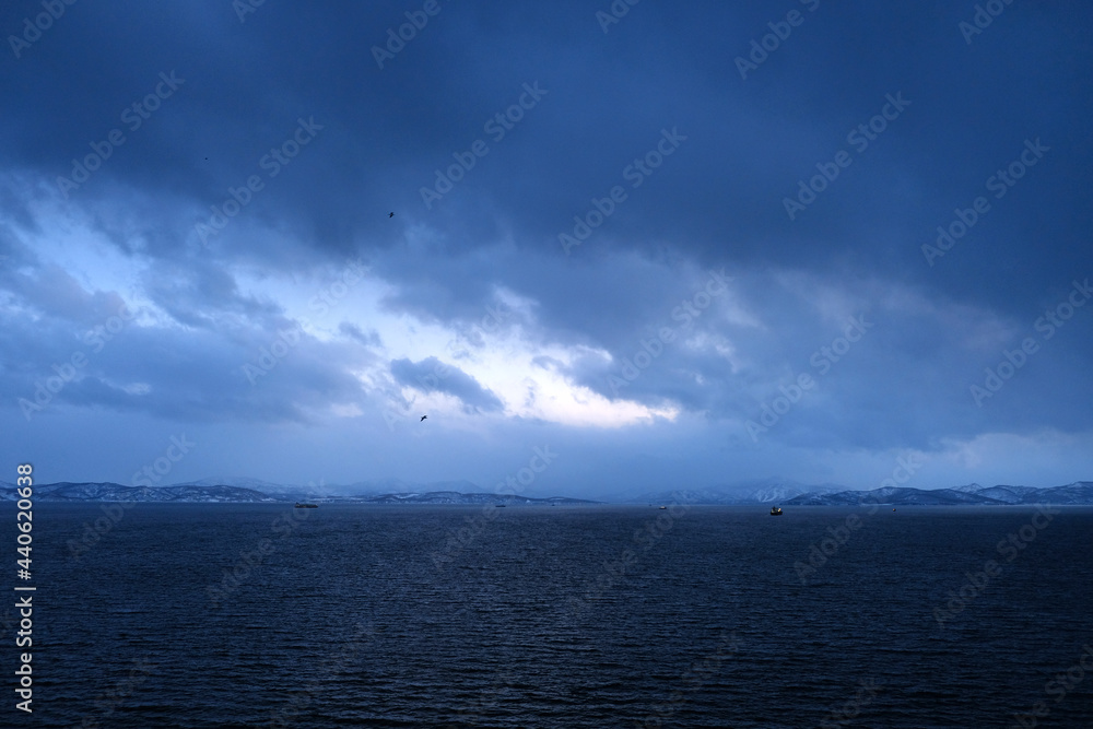 Cloudy evening view of the Avacha Bay. Ships standing in the roadstead, mountains in the background. Petropavlovsk-Kamchatsky, Kamchatka Peninsula, Russia Cloudy evening view of the Avacha Bay. Ships standing in the roadstead, mountains in the background. Petropavlovsk-Kamchatsky, Kamchatka Peninsula, Russia