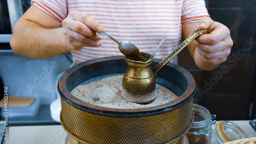 A man brews a Turkish coffee on the sand in the pot, hands close up. Coffee made on the sand in ibrik or ibriq. Coffee in cezve or jezve. Travel inspirational romantic image for web, article, social photo