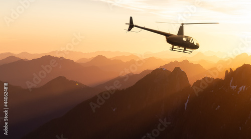 Black Helicopter flying over the Canadian Rocky Mountains. Dramatic Sunrise. Aerial Landscape from British Columbia, Canada in Vancouver Island. Extreme Adventure Composite.
