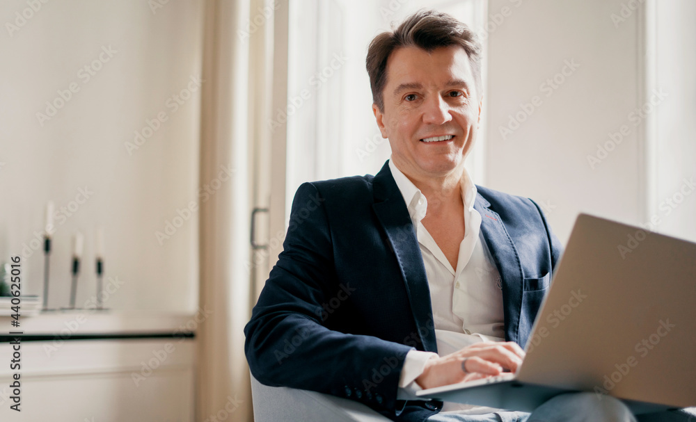 The professional manager smiles and writes a message to the client by email. An adult man in a suit with gray hair works in an office in a coworking. The professional manager smiles and writes a message to the client by email. An adult man in a suit with gray hair works in an office in a coworking.