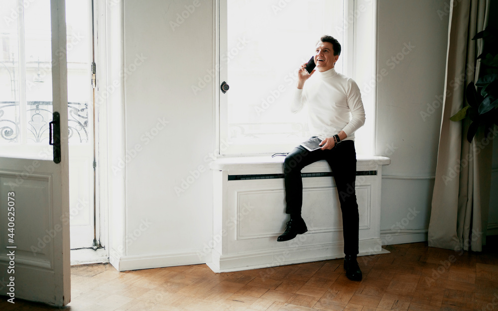 talking on the phone and standing near the window. the work done on the new startup. A designer in a comfortable modern suit looks at the computer. Portrait of an adult creative person. talking on the phone and standing near the window. the work done on the new startup. A designer in a comfortable modern suit looks at the computer. Portrait of an adult creative person.