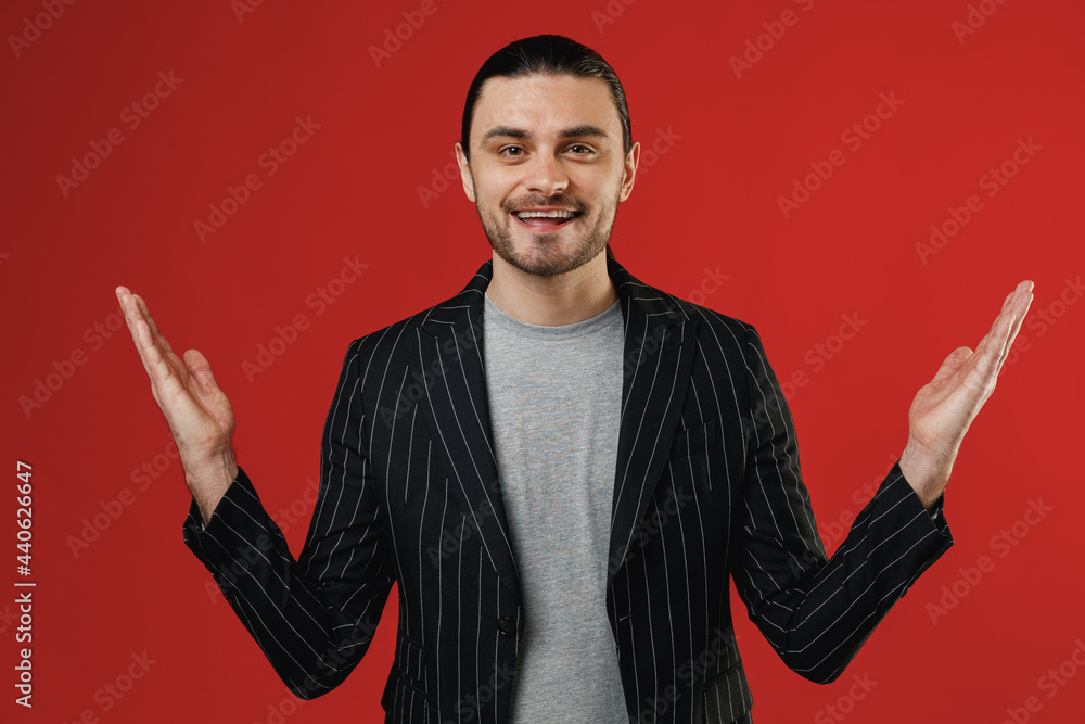 Young smiling surprised businessman latin man 20s long hair ponytail wear black striped jacket grey shirt looking aside isolated on red color background studio portrait. Concept of people lifestyle. Young smiling surprised businessman latin man 20s long hair ponytail wear black striped jacket grey shirt looking aside isolated on red color background studio portrait. Concept of people lifestyle.