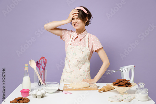 Foto Young housewife housekeeper chef cook baker woman in pink apron work at table kitchenware put hand face facepalm epic fail mistaken isolated on pastel violet background