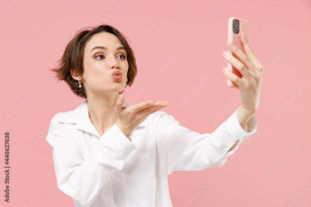 Young employee business woman corporate lawyer in classic formal white shirt work in office do selfie shot mobile phone post photo on social network blow air kiss isolated on pastel pink background. Young employee business woman corporate lawyer in classic formal white shirt work in office do selfie shot mobile phone post photo on social network blow air kiss isolated on pastel pink background.