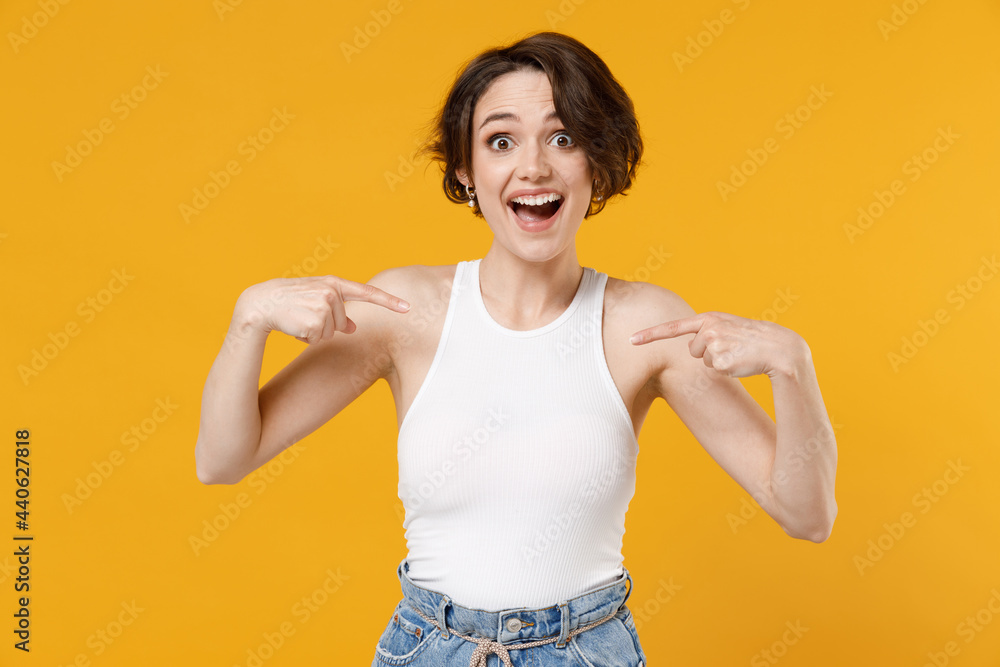 Young excited surprised amazed caucasian woman 20s with bob haircut wearing white tank top shirt point index finger on herself isolated on yellow background studio portrait. People lifestyle concept Young excited surprised amazed caucasian woman 20s with bob haircut wearing white tank top shirt point index finger on herself isolated on yellow background studio portrait. People lifestyle concept