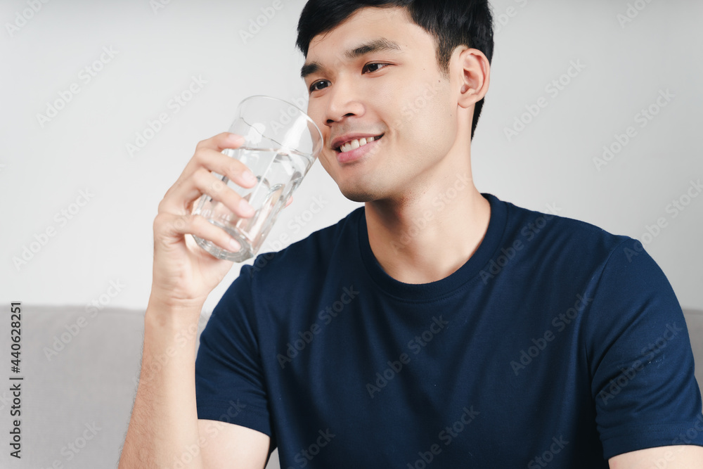 handsome asian man drinking a glass of water on the sofa at living room . handsome asian man drinking a glass of water on the sofa at living room .