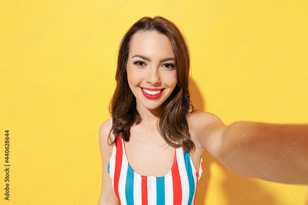 Fototapeta premium Close up happy fun young sexy woman slim body wear striped red blue one-piece swimsuit doing selfie shot isolated on vivid yellow color background studio. Summer hotel pool sea rest sun tan concept.