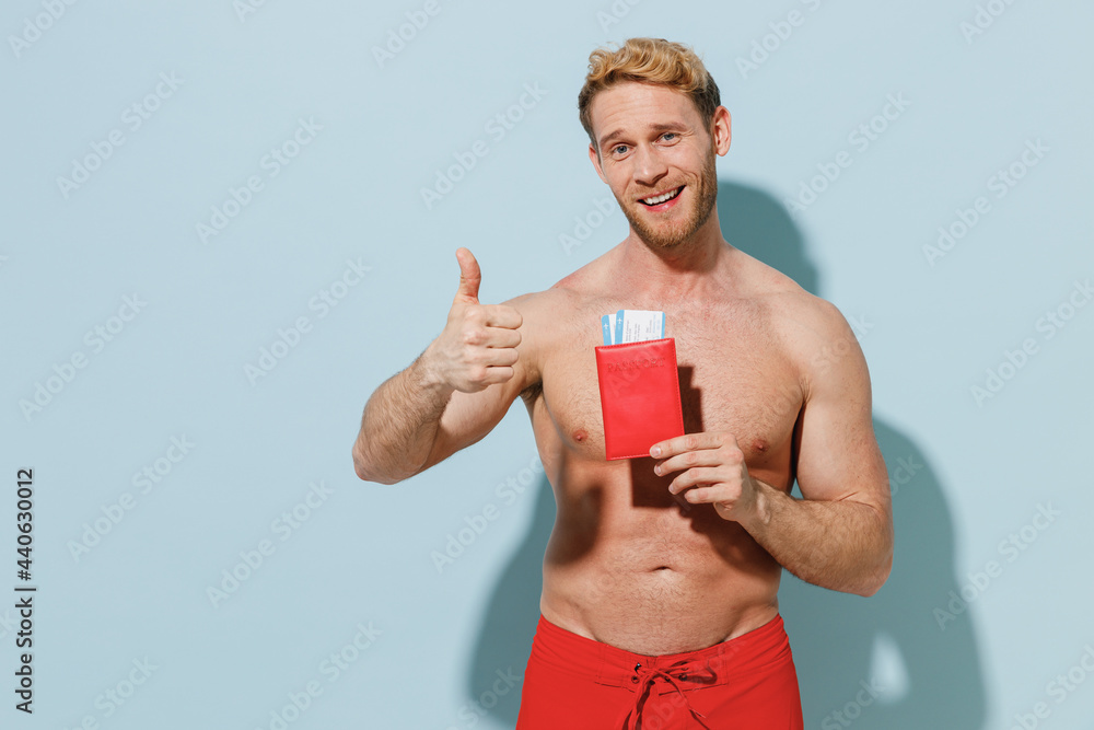 Traveler tourist young man in shorts swimsuit hold passport ticket show thumb up gesture isolated on blue background. Passenger travel abroad weekend getaway. Air flight vacation sea journey concept. Traveler tourist young man in shorts swimsuit hold passport ticket show thumb up gesture isolated on blue background. Passenger travel abroad weekend getaway. Air flight vacation sea journey concept.