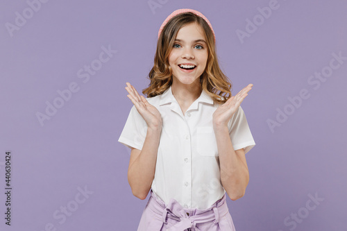 Little surprised amazed caucasian blonde kid girl 12-13 years old in white short sleeve shirt spread hands isolated on purple color background children studio portrait. Childhood lifestyle concept