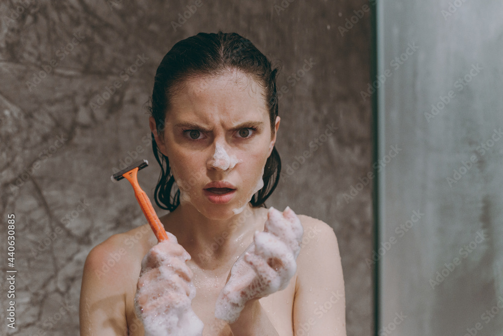 Obraz premium Indignant angry half naked topless young wet haired woman 20s take shower with shampoo gel foam hold razor look camera in bathroom in brown background Skin care healthcare cosmetic procedures concept.