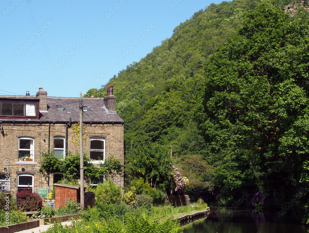 a canal path surrounded by summer flowers with a row of old stone houses at eastwood in hebden bridge west yorkshire