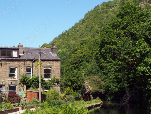 a canal path surrounded by summer flowers with a row of old stone houses at eastwood in hebden bridge west yorkshire photo