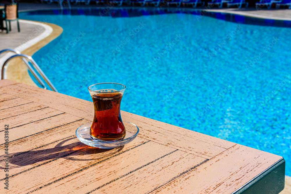 Black tea in traditional turkish glass on table near the swimming pool Black tea in traditional turkish glass on table near the swimming pool