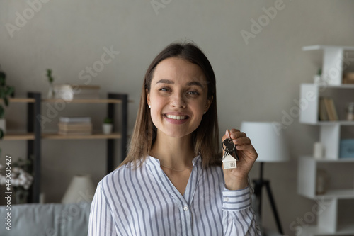 Sincere happy young woman holding key in hands  looking at camera. Joyful candid millennial homeowner feeling excited of purchasing own apartment or new dwelling  satisfied with real estate service.