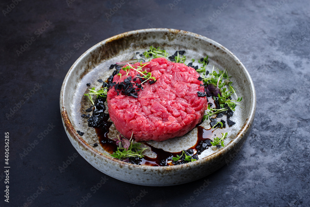 Modern style gourmet tartar raw from beef filet with herbs and spices served as close-up on a Nordic design plate with copy space