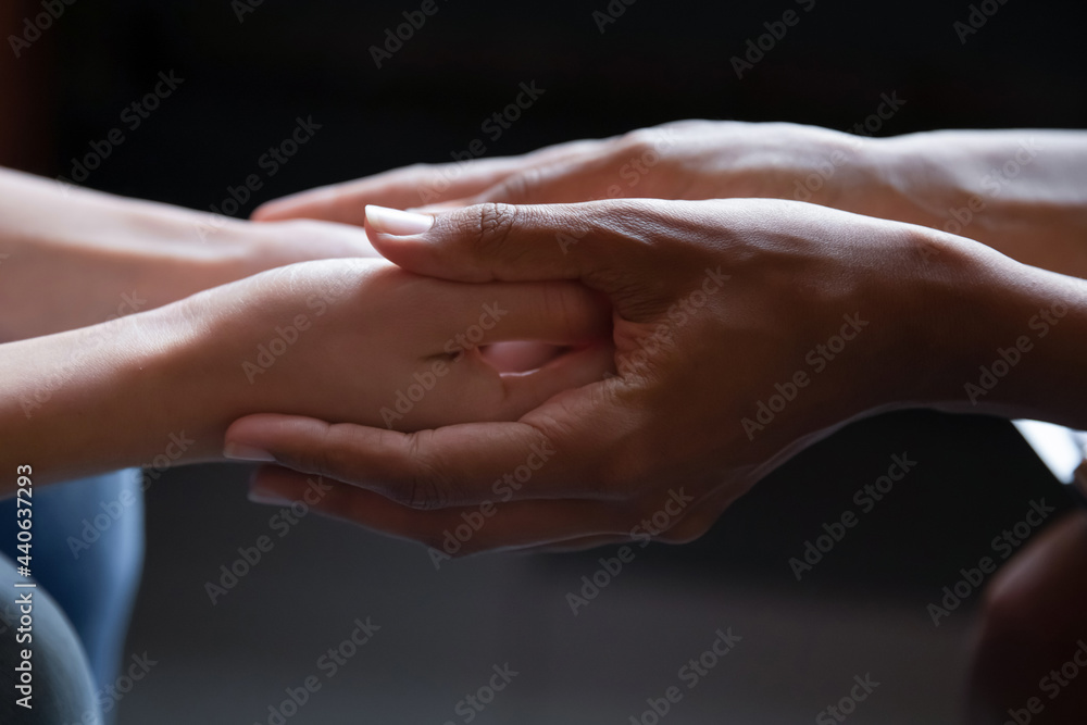 Close up young african american woman holding hand of female caucasian friend, giving psychological help, supporting in difficult life situation. Sincere mixed race people holding trusted conversation