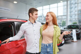 Happy beautiful woman hugging with her boyfriend, celebrating buying new car together at the dealership