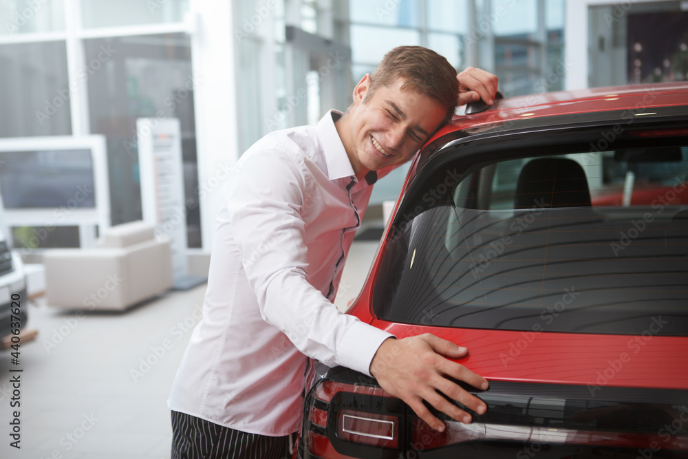Young man laughing excitedly, hugging his new automobile at car dealership