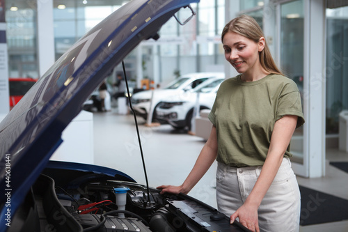 Female driver looking under car hood, choosing automobile to buy at the dealership
