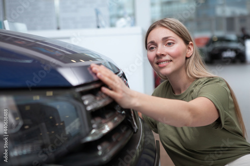 Beautiful woman examining new car at auto dealership, looking for auto to buy