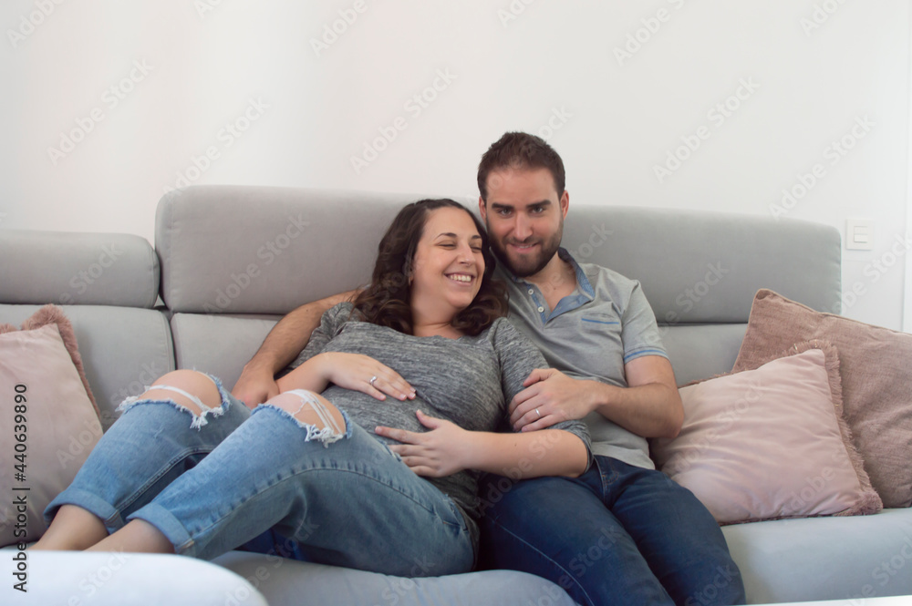 Pregnant wedding couple sitting on a sofa looking at each other and smiling Pregnant wedding couple sitting on a sofa looking at each other and smiling