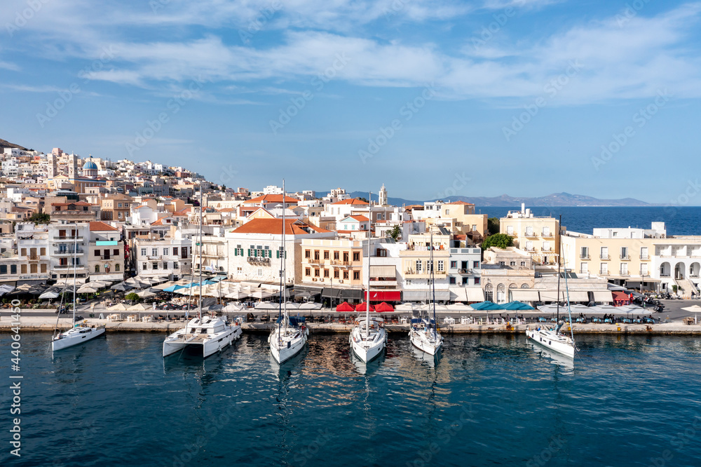 Syros island, Greece, aerial drone view. Saiboats moored at port dock, yachts marina. Ermoupolis town buildings background.