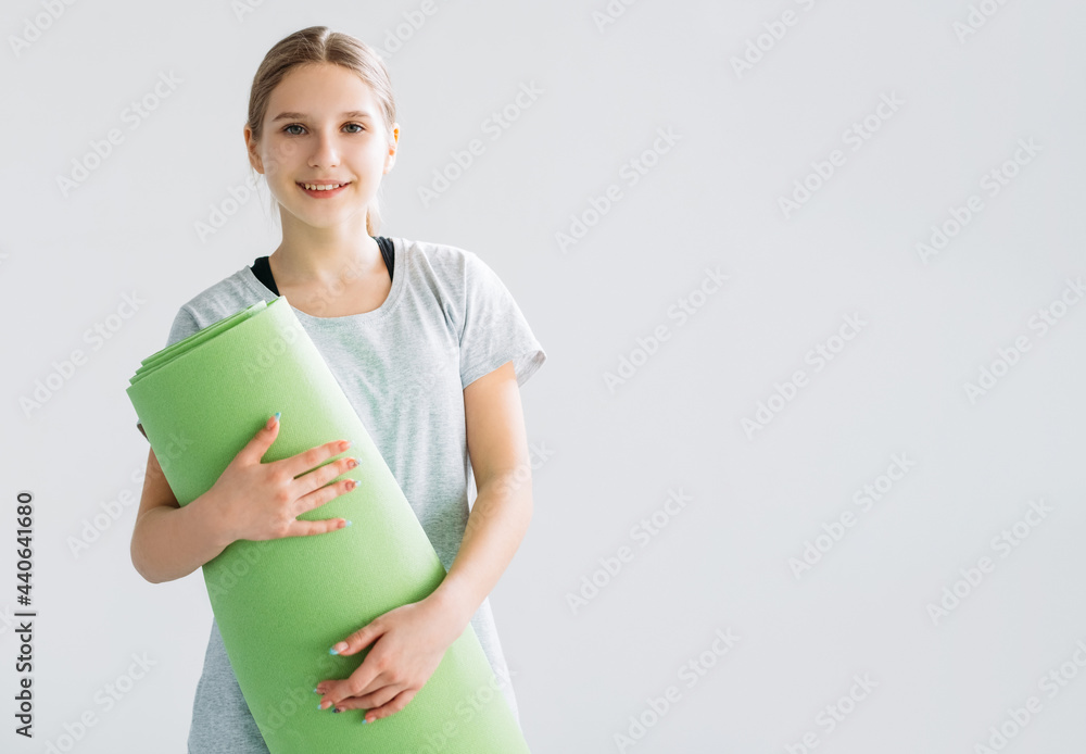 Fitness accessories. Active kids. Fitness training equipment. Smiling satisfied athletic girl showing thumb up like gesture with green yoga mat isolated on light copy space background.