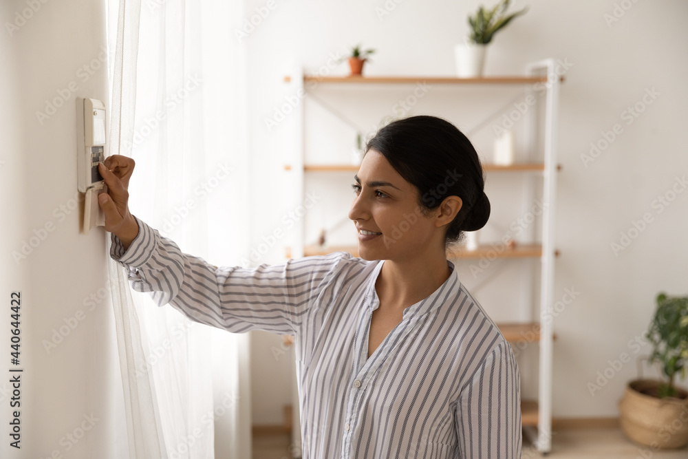 Happy millennial Indian woman press button activate smart home system at home. Smiling young mixed race female use modern security equipment or alarm control panel indoors. Technology concept. Happy millennial Indian woman press button activate smart home system at home. Smiling young mixed race female use modern security equipment or alarm control panel indoors. Technology concept.