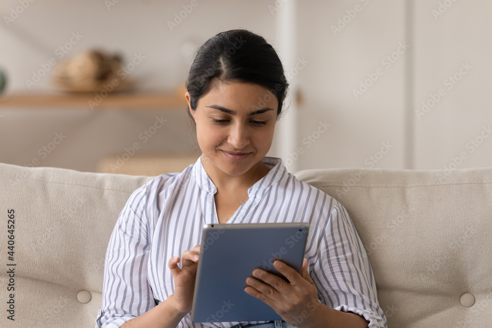 Smiling millennial Indian female relax at home use modern pad gadget browse wireless internet. Happy young mixed race woman hold tablet talk on webcam video call. Technology, commination concept. Smiling millennial Indian female relax at home use modern pad gadget browse wireless internet. Happy young mixed race woman hold tablet talk on webcam video call. Technology, commination concept.