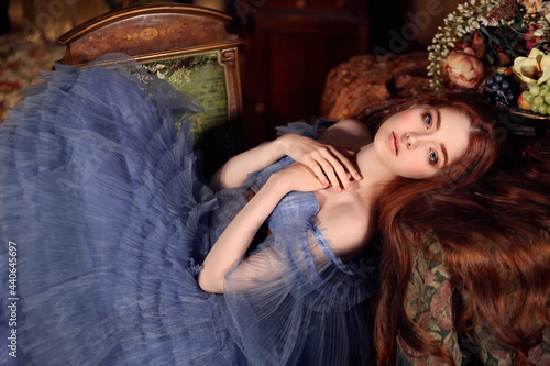 Bild auf Leinwand Beautiful girl with long red hair in blue evening dress laying on the chair in v